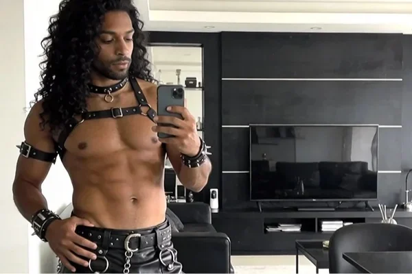man with long curly hair and leather straps takin mirror selfie